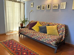 Una habitación con sofá, alfombra estampada, planta en maceta y cuadros en la pared.