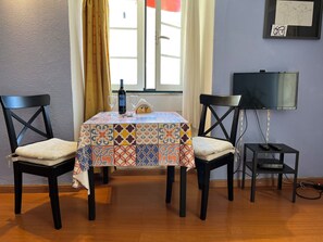Un comedor con una mesa, sillas, una botella, vasos, un televisor y una pared decorada con dibujos.