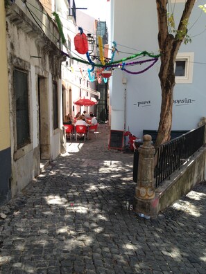 A narrow cobblestone street with outdoor seating, a tree, and a building with a sign.