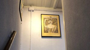 Een trap met een houten leuning, een lijstwerk met een kunstwerk aan de muur, en een lamp erboven.