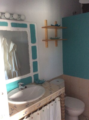 Ein Badezimmer mit Waschbecken, Spiegel und Toilette. Über dem Waschbecken befindet sich ein Handtuchhalter und ein Regal mit einem darüber hängenden Handtuch.
