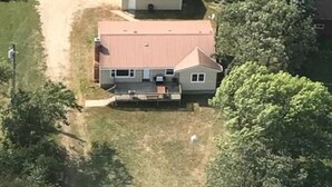 A two-story house with a red roof, a front yard, and a dirt driveway.