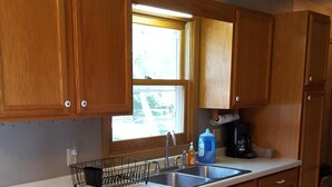 A kitchen with wooden cabinets, a sink, a window, and a coffee maker.
