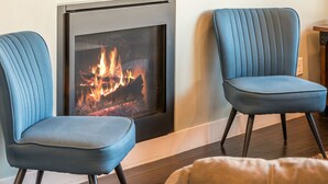 Ein Zimmer mit Kamin, zwei blau gepolsterten Sesseln und einem braunen Ledersitzhocker.