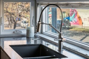 A kitchen with a stainless steel sink, a window with a view of a street and a mural, and a mosaic-patterned container on the counter. - Dream Pad: 3BR Townhouse-heart of RiNo w/ private garage - Sleeps 10! (Denver)