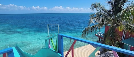 A wooden deck with a blue railing overlooking clear turquoise water.