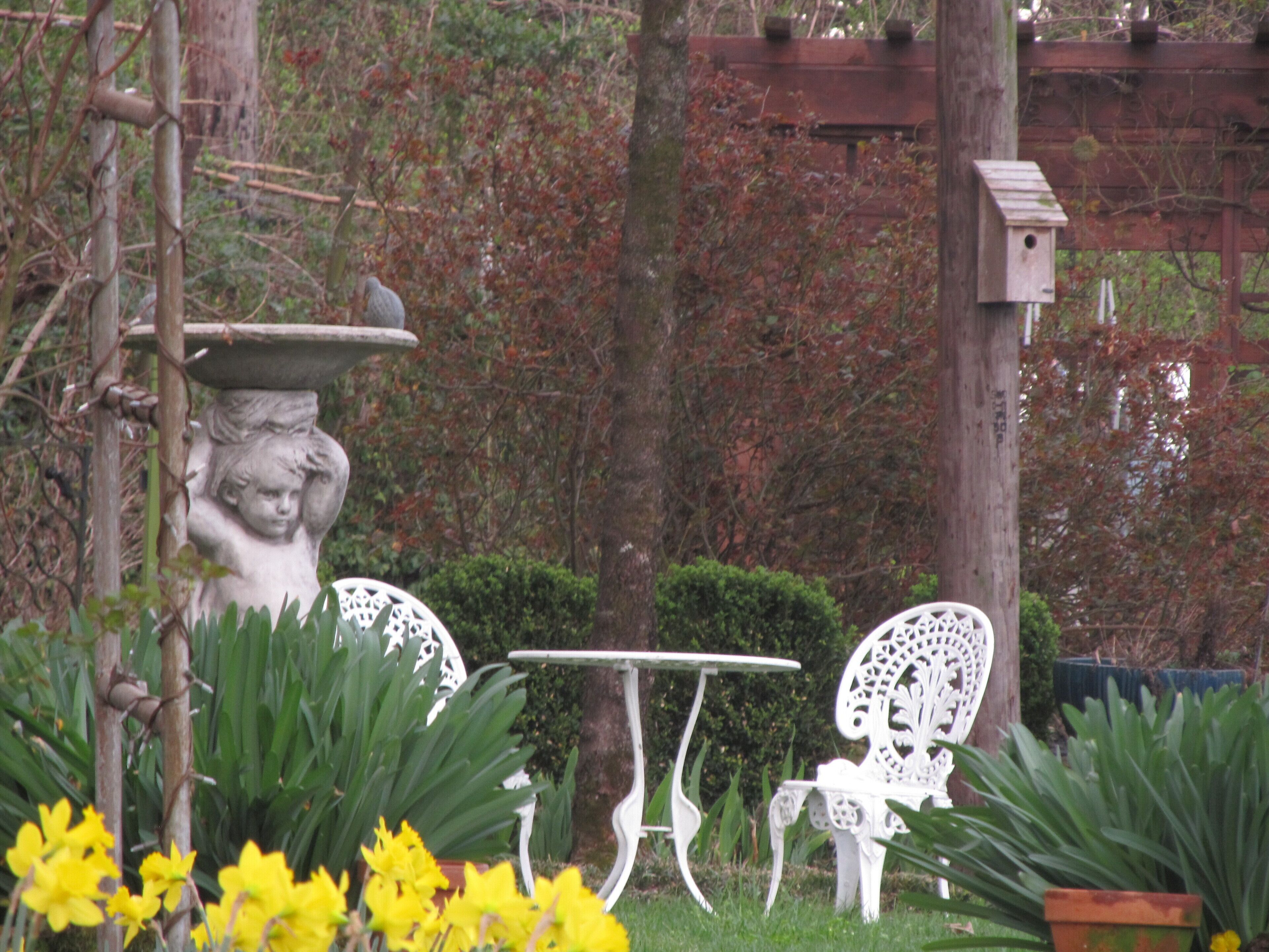 Un jardin avec une nichoir blanc, une table blanche et deux chaises blanches.