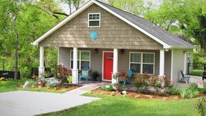 Ein eingeschossiges Haus mit roter Tür, einer Veranda und einem kleinen Garten mit roten Blumen.