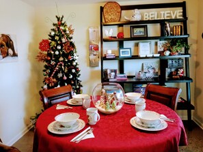 Un coin repas avec une nappe rouge, un sapin de Noël et une bibliothèque remplie de divers objets.
