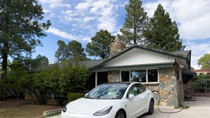 En hvid Tesla holder foran et hus med facade af sten og træ.