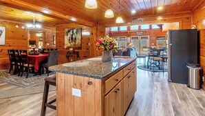 A wooden cabin interior with a kitchen, dining area, and a large island with a vase of flowers. -  7 person new HOT TUB  at Stunning Log Cabin 4 bed 4 full bath  5 min  to TI (Rutherfordton)