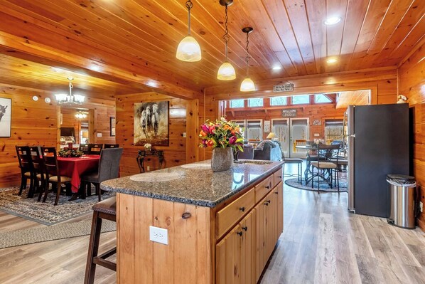 A wooden cabin interior with a kitchen, dining area, and a large island with a vase of flowers. -  7 person new HOT TUB  at Stunning Log Cabin 4 bed 4 full bath  5 min  to TI (Rutherfordton)