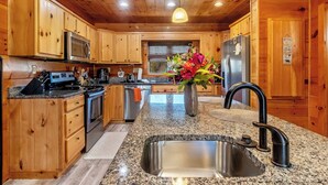 A modern kitchen with wooden cabinets, granite countertops, stainless steel appliances, and a large sink. -  7 person new HOT TUB  at Stunning Log Cabin 4 bed 4 full bath  5 min  to TI (Rutherfordton)
