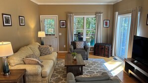 A living room with a beige sofa, a grey armchair, a wooden coffee table, and a television. - Nestled Among Majestic Trees, Hilltop Hideaway is a Woodland Sanctuary (Amissville)
