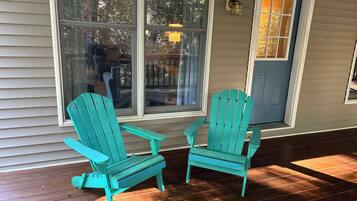 Dos sillas Adirondack turquesa en una terraza de madera frente a una casa con revestimiento beige y una puerta azul.