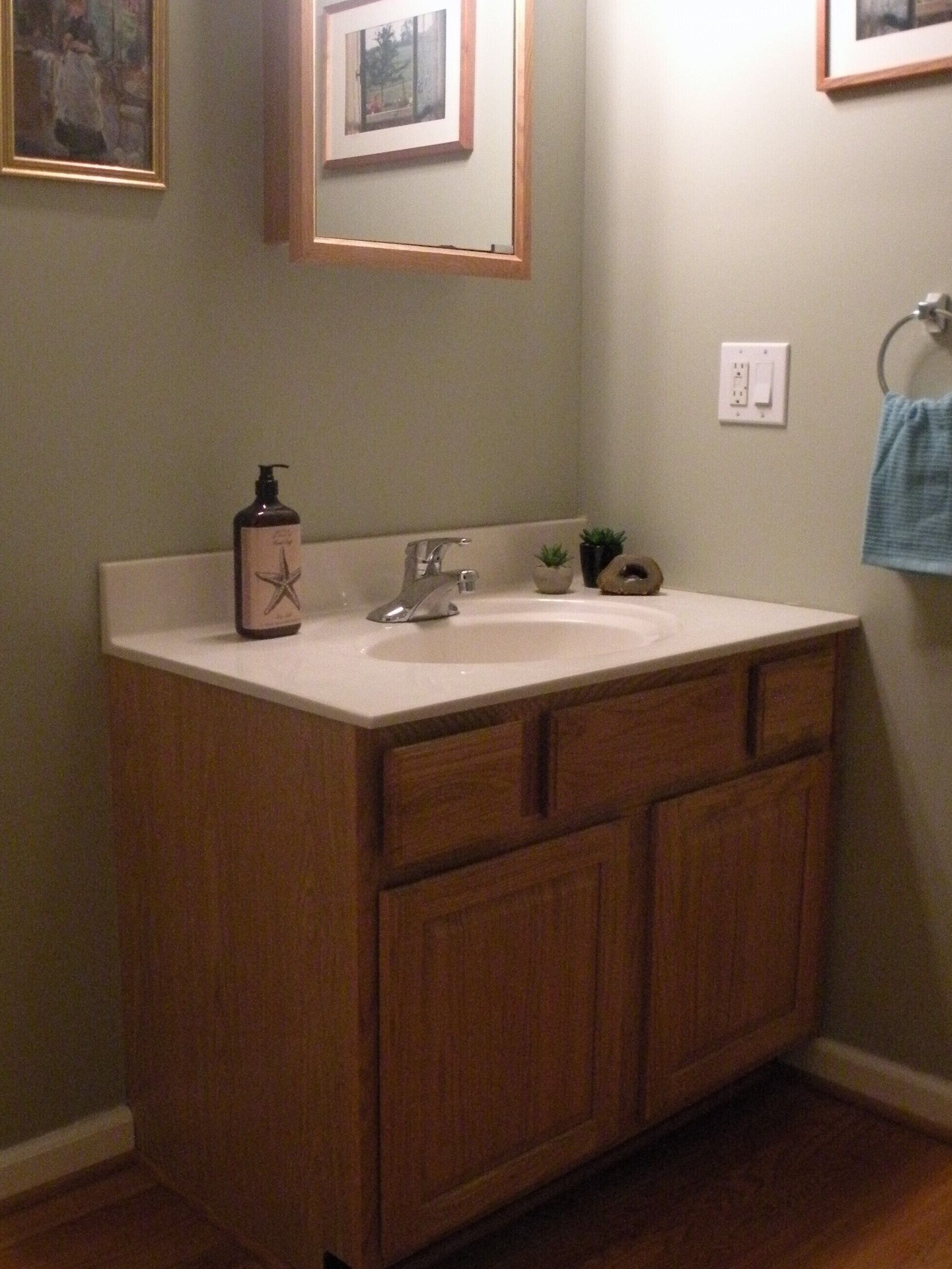 A bathroom with a wooden vanity, a sink, a mirror, and framed pictures on the wall.