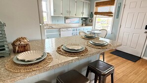 A kitchen with a central island, bar stools, and a dining area with chairs. - Semi oceanfront location with a 3 min walk to the ocean and Gift Card (Nags Head)