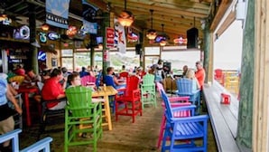 An outdoor restaurant with colorful chairs and tables, a wooden deck, and a view of the ocean. - Semi oceanfront location with a 3 min walk to the ocean and Gift Card (Nags Head)