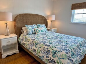 Ein Schlafzimmer mit einem großen Bett, zwei Nachttischen, einem Rattan-Kopfstück und einem Fenster mit Blick.