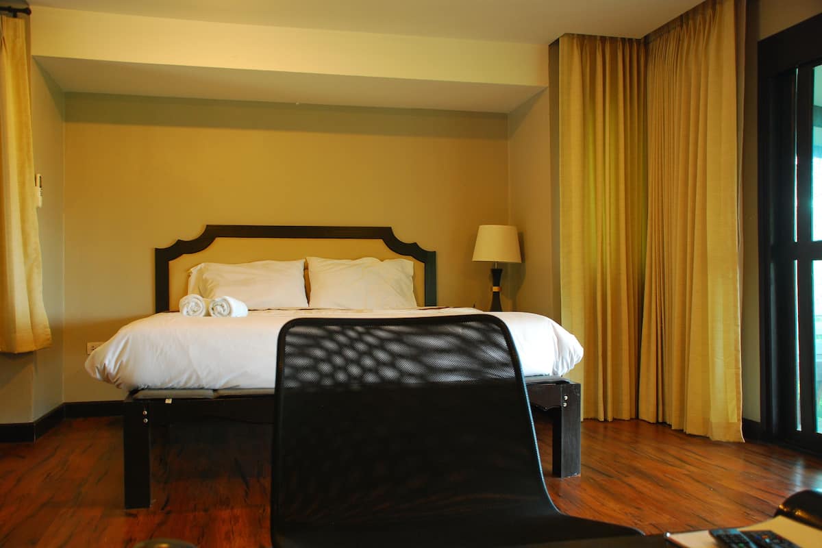 A hotel room with a bed, a chair, a lamp, and curtains.