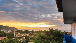A residential area with a view of the sunset over the ocean, surrounded by greenery and buildings. - Hostal Alcazaba (Puerto Lopez)