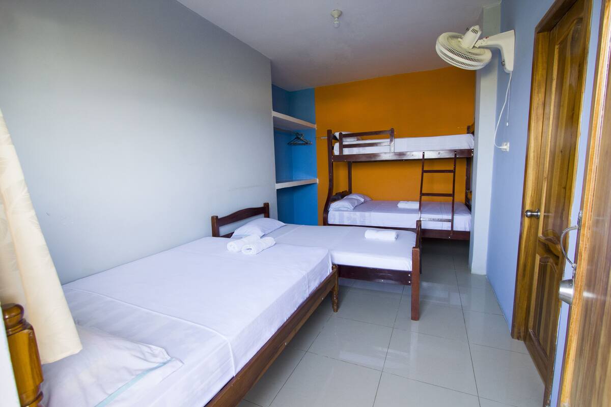 A dormitory room with two bunk beds, a ceiling fan, and a door.