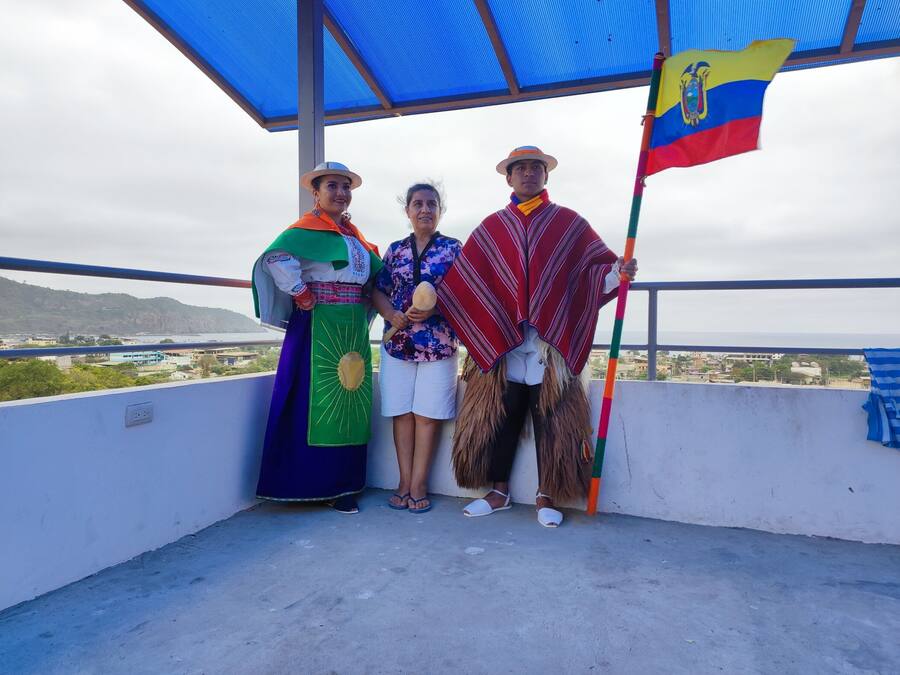 A balcony with a view of a coastal city, a flag, and people in traditional attire.
