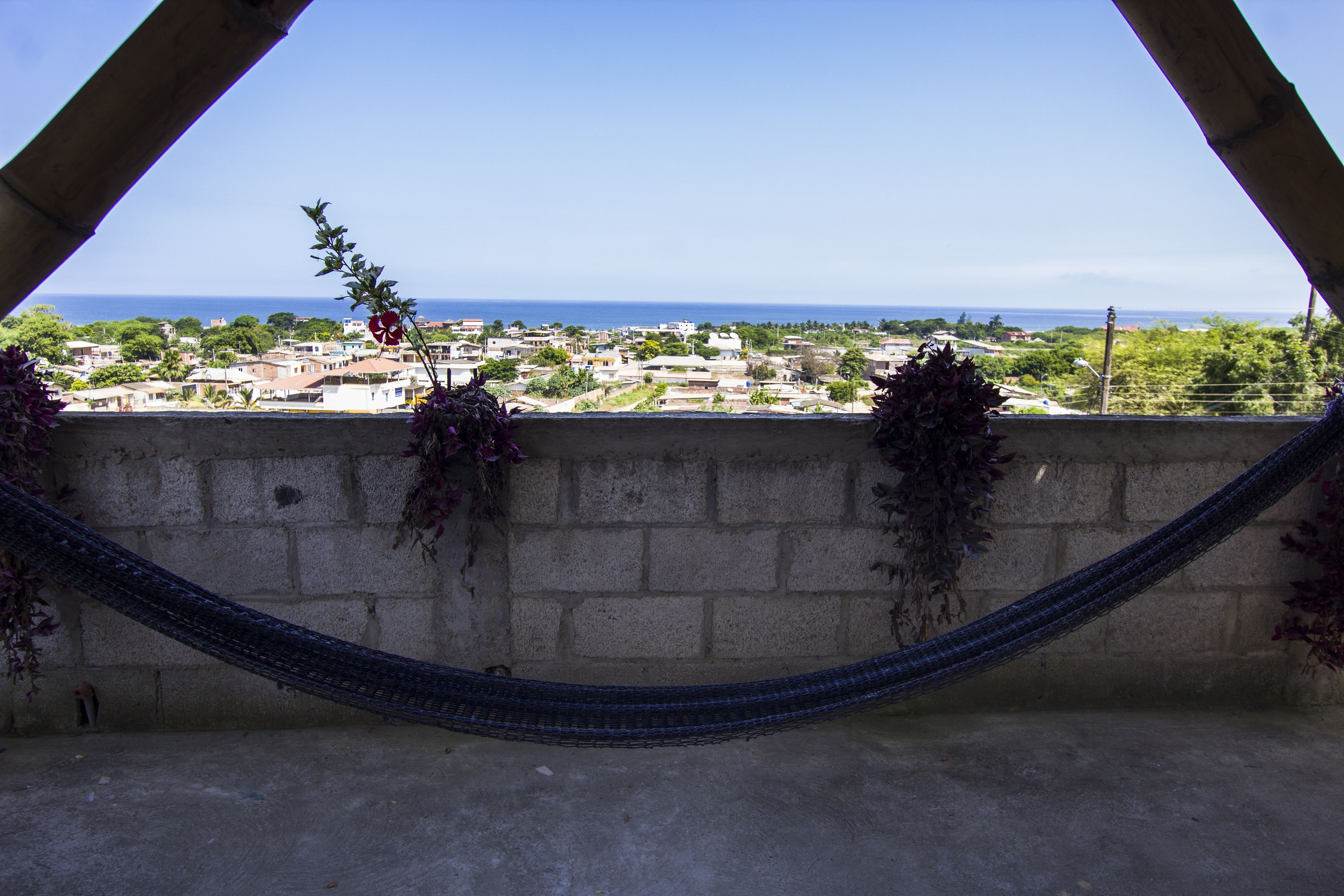 A hammock tied between two concrete walls overlooking a coastal town with buildings and greenery.
