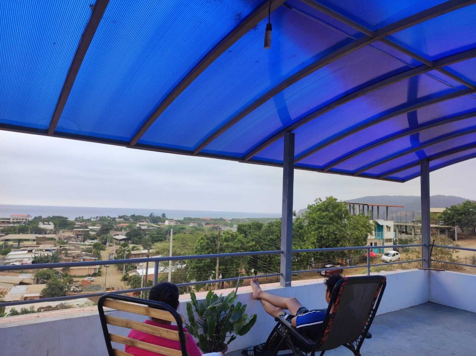A balcony with a blue canopy overlooking a residential area.