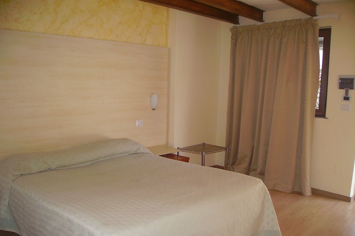 A bedroom with a bed, a small table, and a curtain.