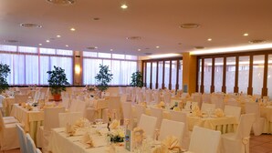 A banquet hall with rows of tables set for a formal event, large windows with sheer curtains, and potted plants. - Camere Angela e Vincenzo (Cava de' Tirreni)