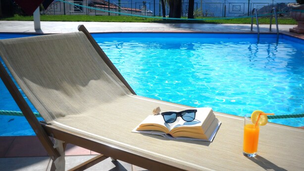 A poolside lounge chair with a book, sunglasses, and a drink. - Camere Angela e Vincenzo (Cava de' Tirreni)