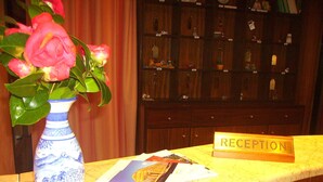 A reception desk with a vase of pink flowers, a sign labeled "RECEPTION," and a marble countertop. - Camere Angela e Vincenzo (Cava de' Tirreni)