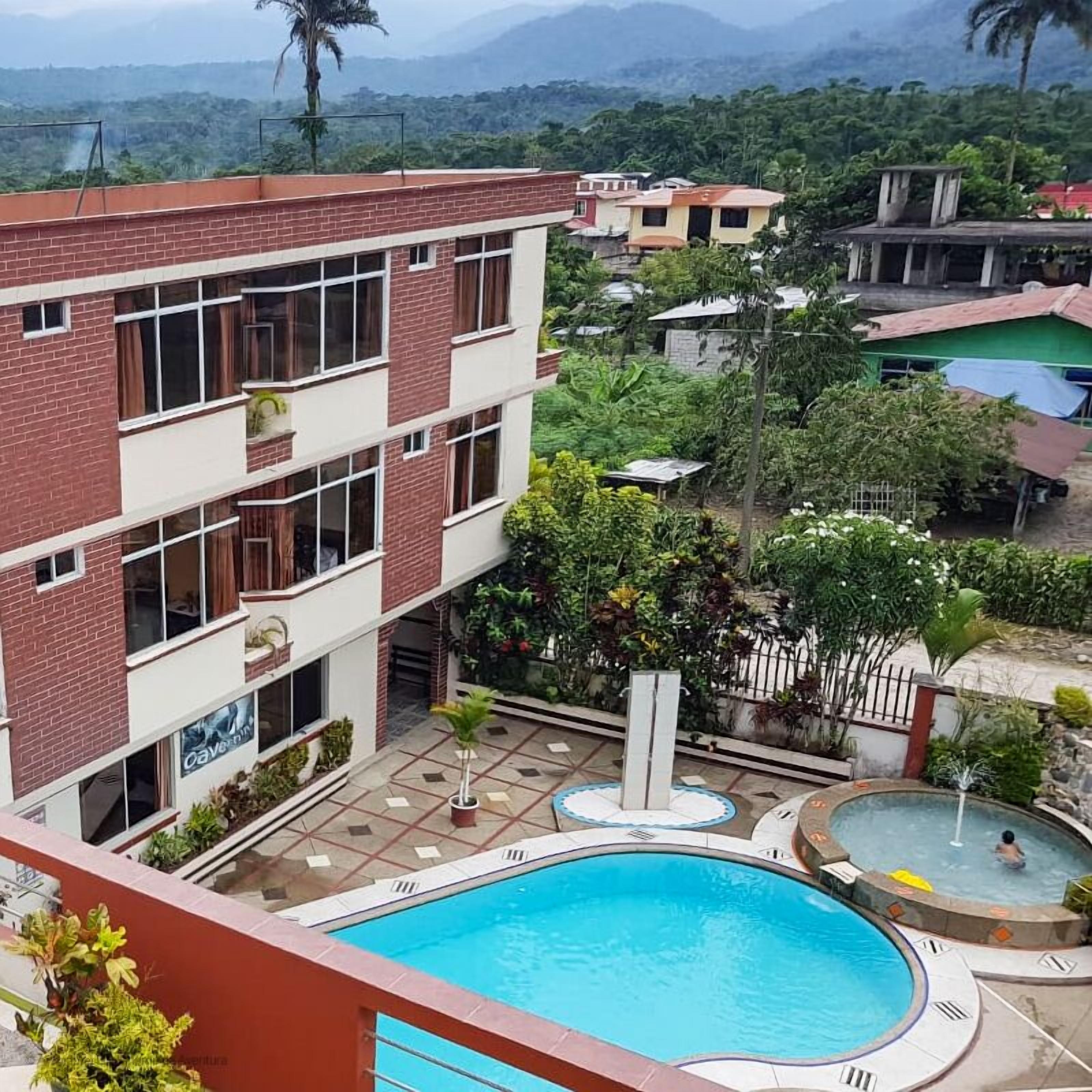 Un edificio de varios pisos con una piscina, rodeado de vegetación y otros edificios.