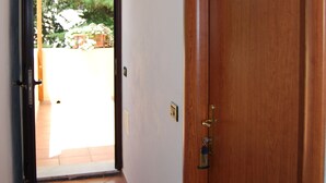Pasillo con puerta de madera numerada con el número 5, que da a un espacio exterior con suelo de baldosas y vistas al verdor.