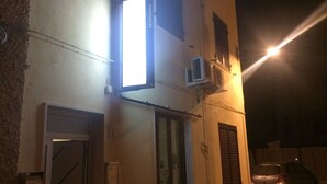 Un edificio de dos plantas con entrada a nivel de calle, una ventana con vistas y un equipo de aire acondicionado en la pared.