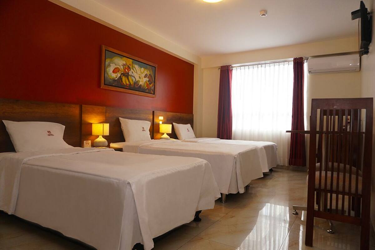 A hotel room with two beds, a painting on the wall, an air conditioning unit, and a wooden chair.