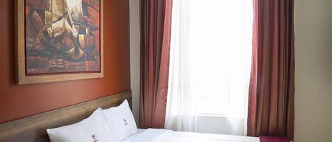 Una habitación de hotel con cama, un cuadro en la pared y cortinas.