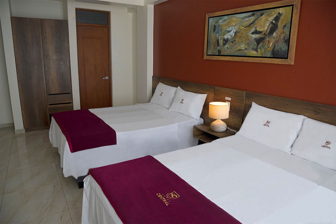 A hotel room with two beds, a wooden wardrobe, a painting on the wall, and a nightstand with a lamp.