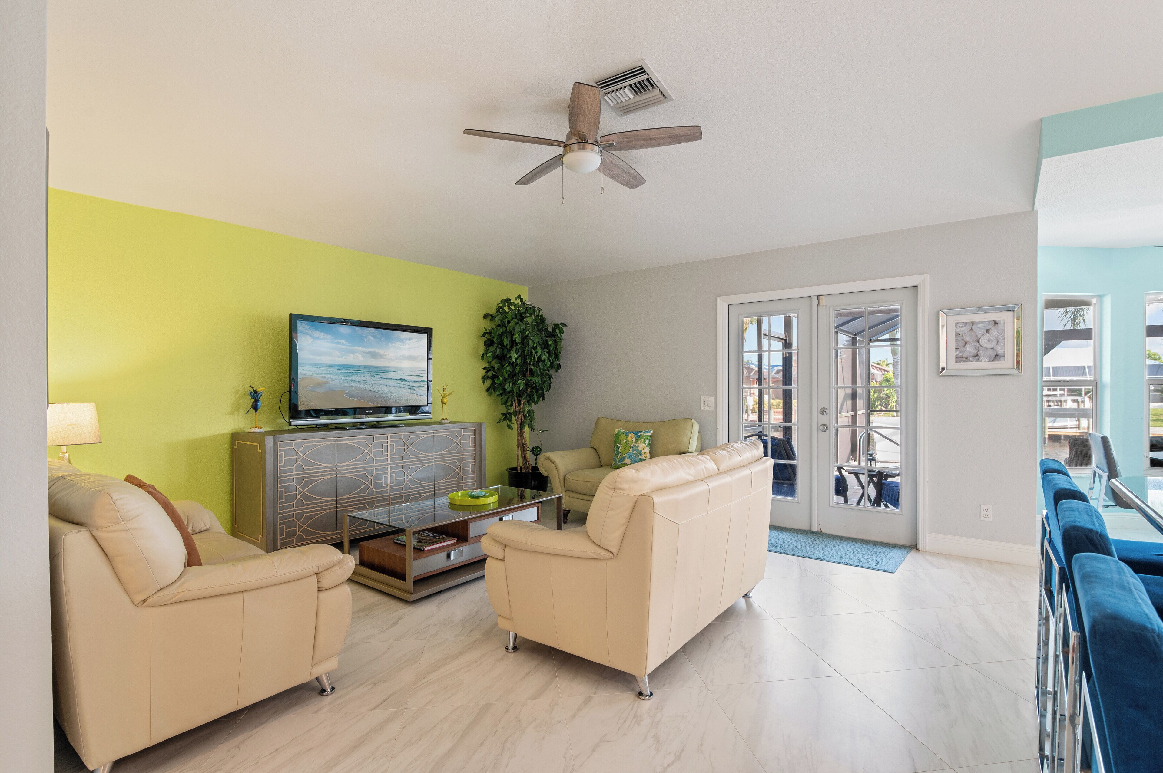 A living room with a beige sofa, a glass coffee table, a television, and a ceiling fan.