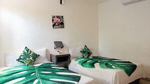 A room with two beds, each with a green leaf-patterned bedspread, a nightstand with a lamp, a wall-mounted air conditioner, and a framed picture above the bed. - Hotel Posada Edem (Cozumel)