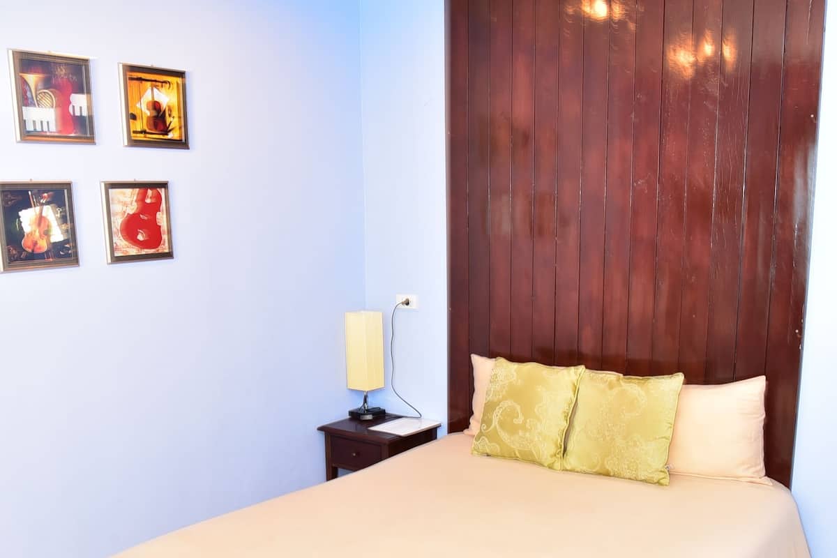 A neatly made bed with a wooden headboard, a bedside table with a lamp, and three framed pictures on the wall.
