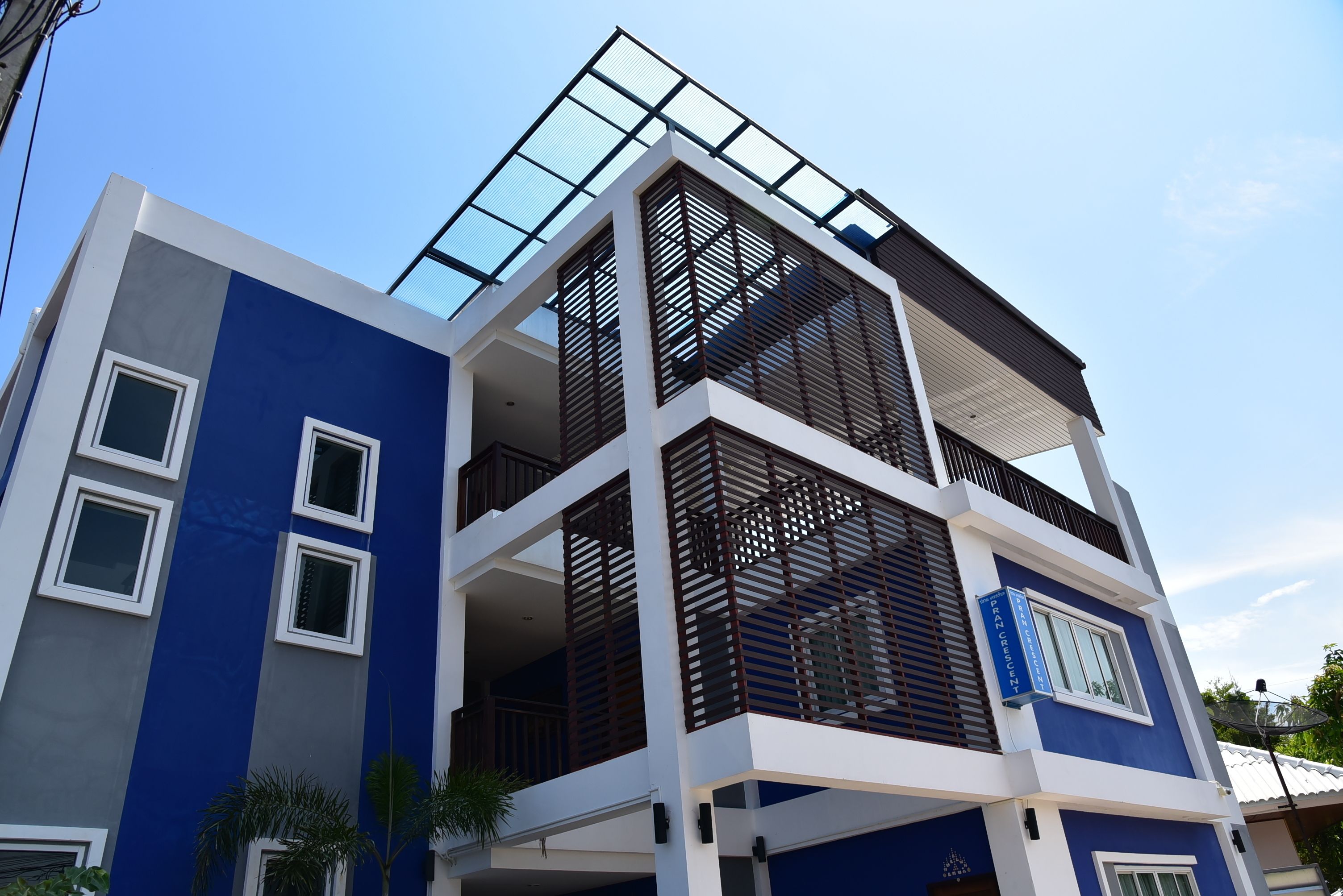 Un edificio moderno de varios pisos con fachada azul, ventanas grandes y un balcón con barandillas de madera.