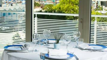 A dining table set for four with a view of the sea and beach through large windows.