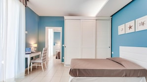 Una camera da letto con un letto, una scrivania e una sedia. Si nota un armadio e una porta che dà su un'altra stanza.