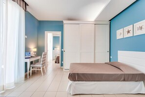 Un dormitorio con cama, escritorio y silla. Hay un armario y una puerta que da a otra habitación.