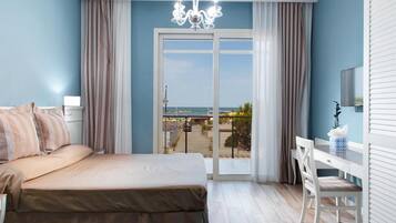 A bedroom with a bed, a desk, and a view of the sea through a glass door.