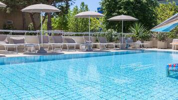 A swimming pool with lounge chairs and umbrellas, surrounded by trees and a building.