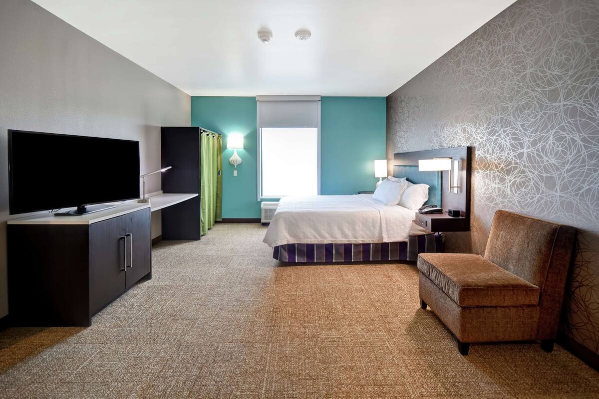 A hotel room with a bed, a TV, a desk, and a chair.