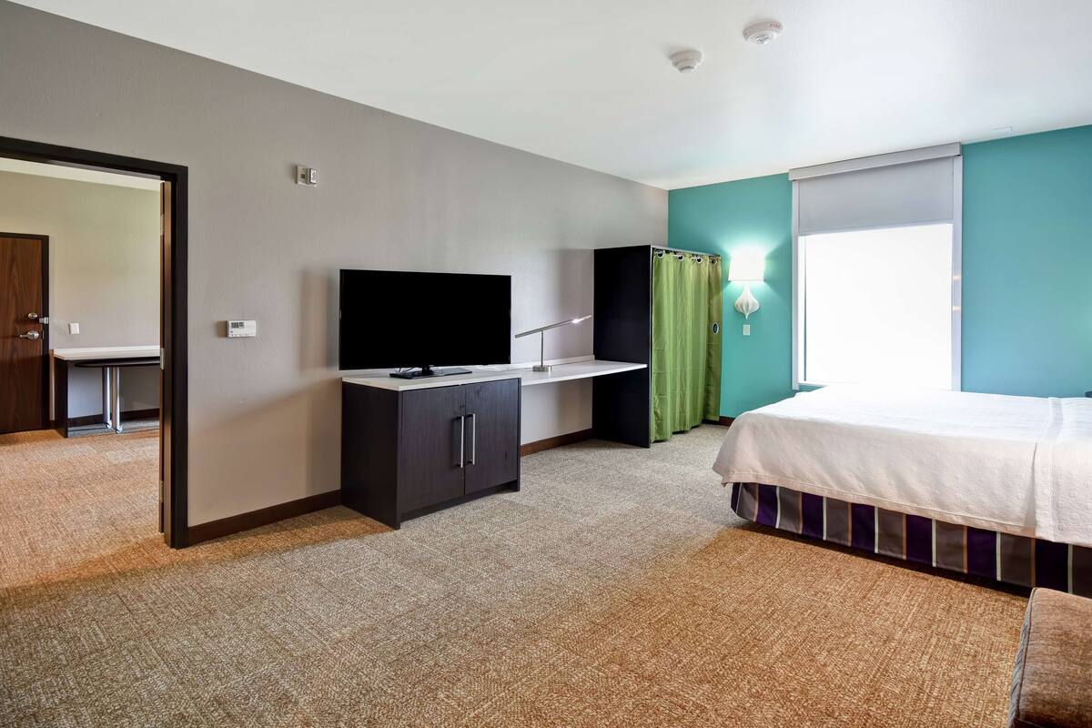 A hotel room with a bed, a desk, a television, a wardrobe, and a bathroom visible through an open door.